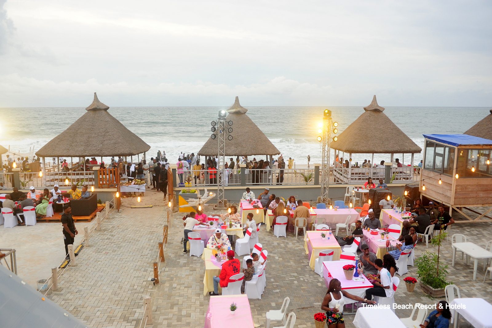 Guests dining under thatched beach huts at sunset beside the Atlantic shoreline