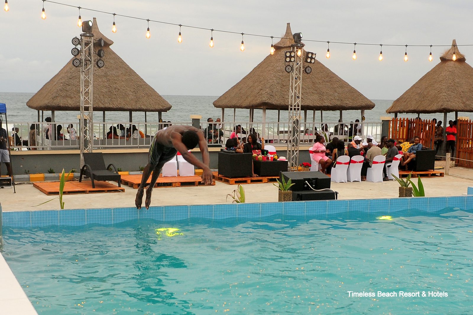 Guest diving into the resort pool with thatched beach huts and the ocean behind