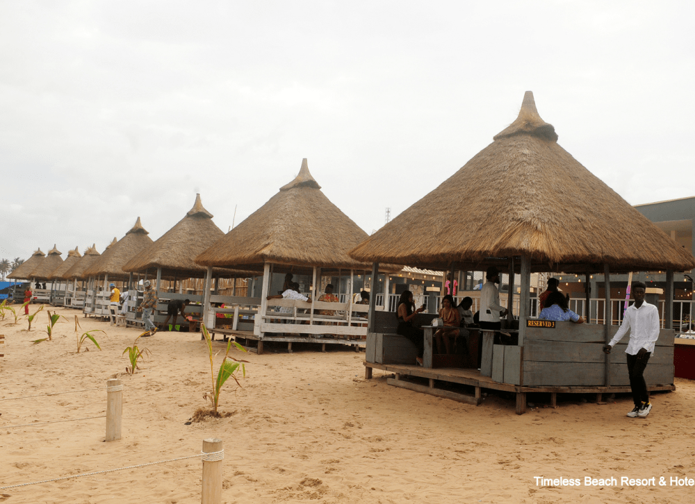 Row of thatched-roof beach cabanas on the sand with guests seated inside
